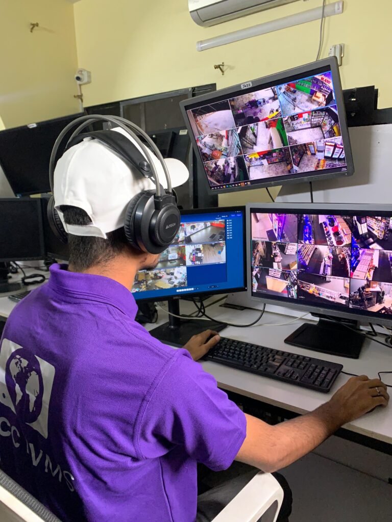 Security technician in a purple GCCTVMS uniform monitoring real-time CCTV footage on multiple screens, providing remote CCTV monitoring services.