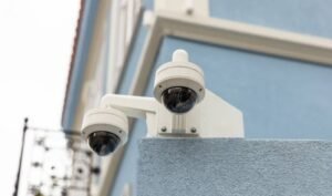 Two white dome-style security cameras mounted on a blue and white building exterior, illustrating the equipment deployed by a professional CCTV monitoring company for commercial sites.