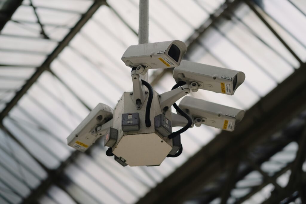 A cluster of four white bullet security cameras mounted on a hexagonal fixture, looking down from a high, glass-panelled ceiling.