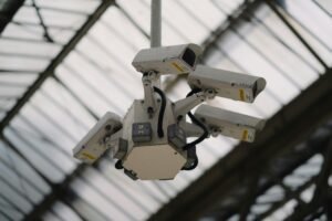 A cluster of four white bullet security cameras mounted on a hexagonal fixture, looking down from a high, glass-panelled ceiling.
