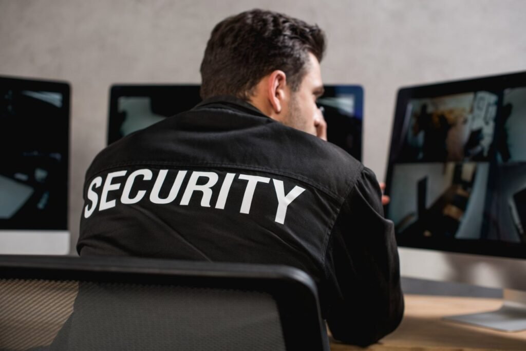 A security guard in a black uniform actively reviewing live video feeds on multiple computer screens, representing the professional human expertise that determines overall CCTV Monitoring Costs in USA for reliable cctv monitoring and security system monitoring.