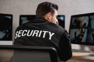 A security guard in a black uniform actively reviewing live video feeds on multiple computer screens, representing the professional human expertise that determines overall CCTV Monitoring Costs in USA for reliable cctv monitoring and security system monitoring.