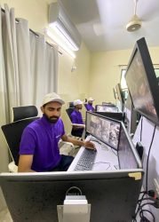 Team members in purple GCCTVMS uniforms monitoring real-time CCTV footage on computer screens in a control room.