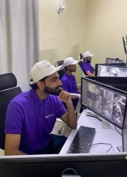 Three operators in purple GCCTVMS uniforms seated at computers, monitoring multiple CCTV camera feeds.