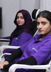 Two female team members in purple GCCTVMS uniforms seated at computers, monitoring CCTV feeds in a secure environment.